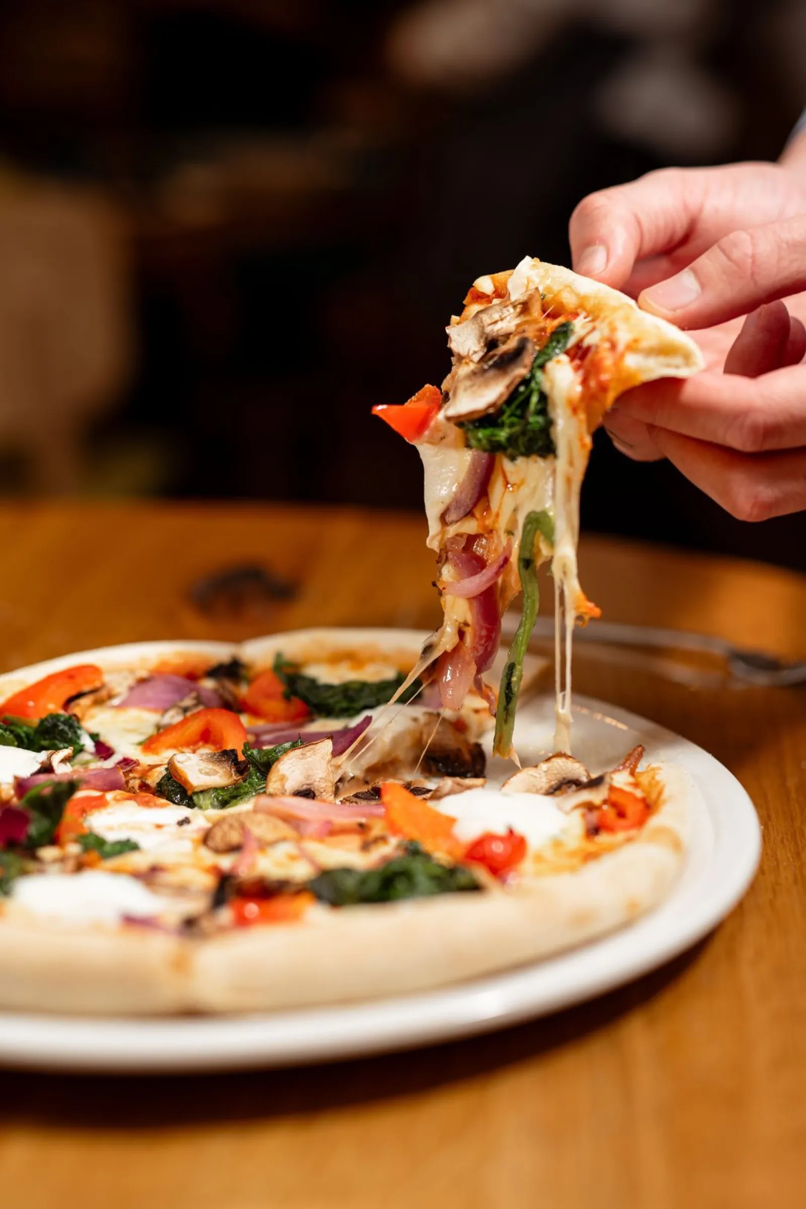 A slice of pizza lifted from the plate, cheese stretching