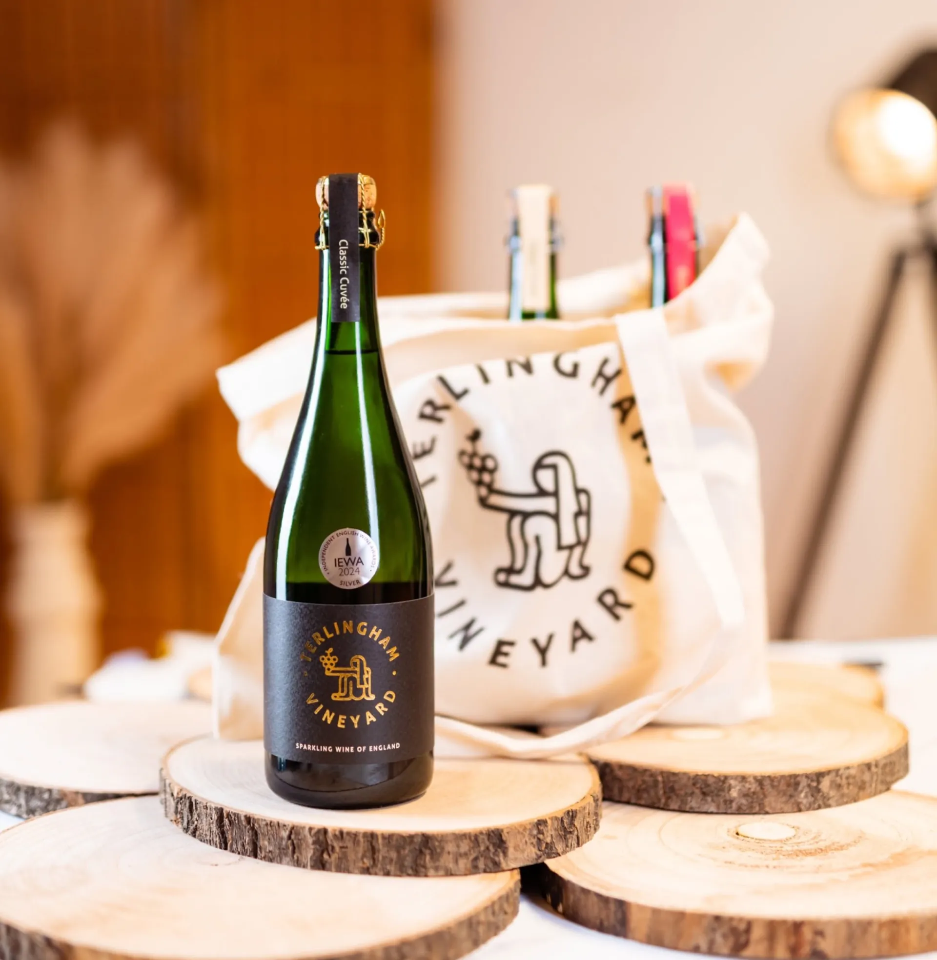 A bottle of Terlingham Classic Cuvée on a log slice, tote bag behind