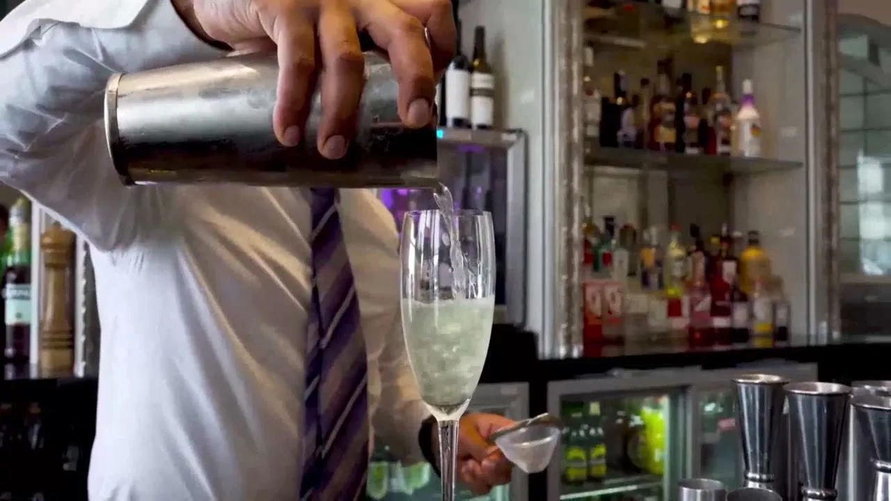 A bartender pouring a cocktail from a shaker into a coupe