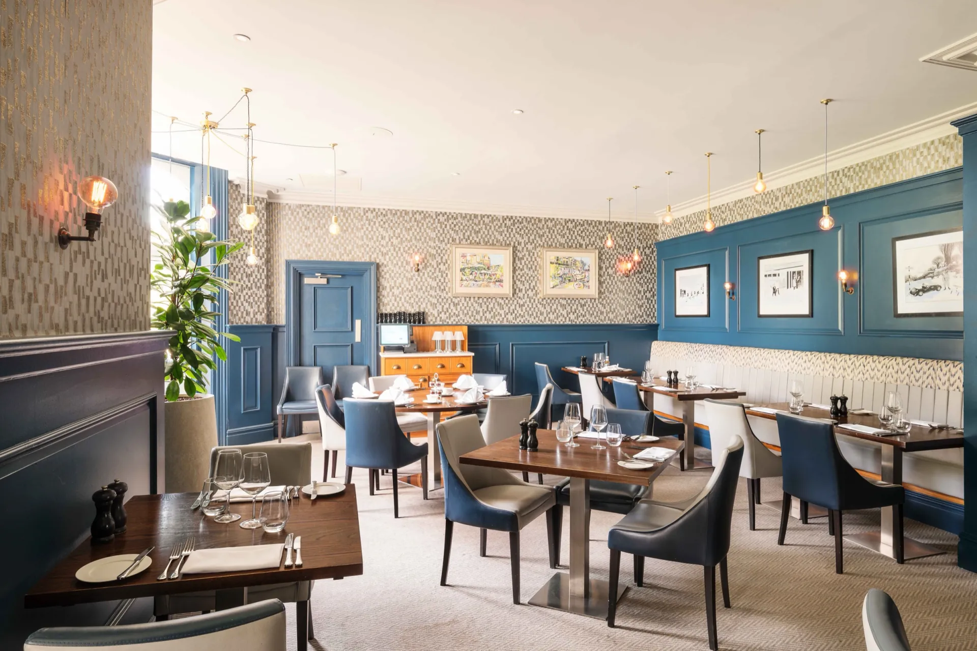 Blue-walled bar and lounge with wooden tables at voco The Clifton